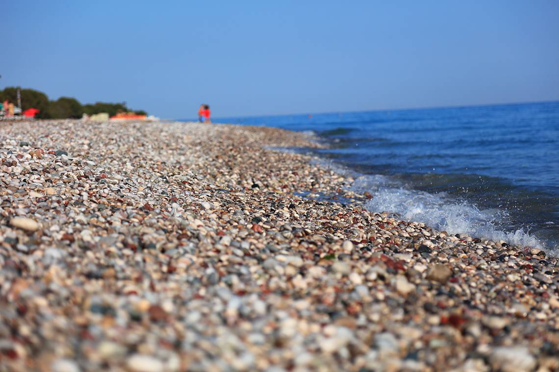 Strand des Blue Bay Beach Resorts mit kleinen Steinen und sanfter Brandung.