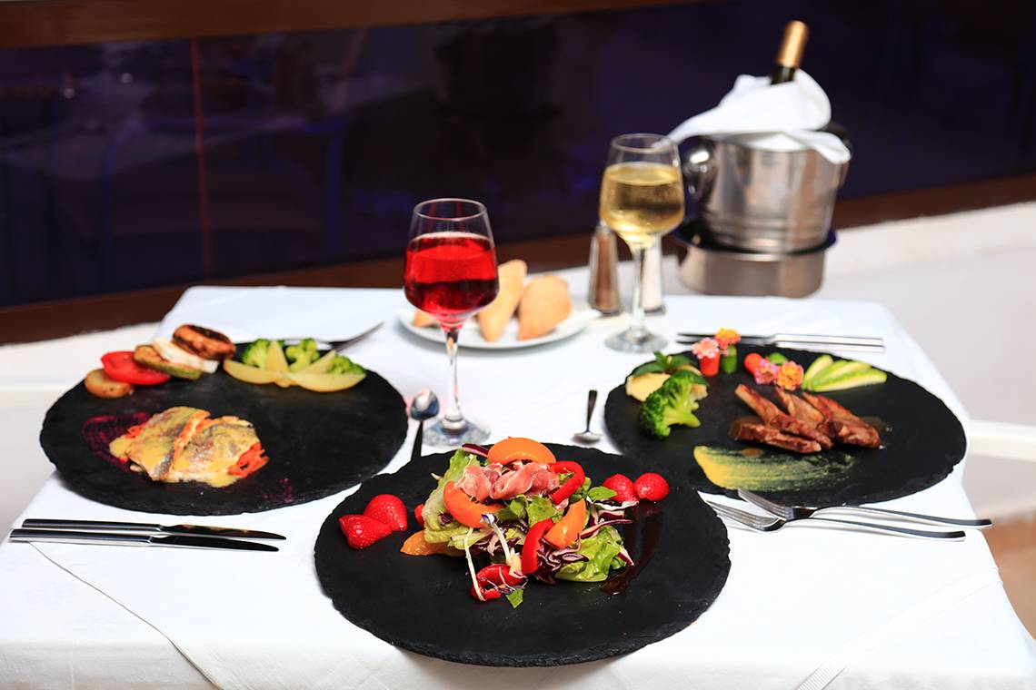 Ein Tisch des Blue Bay Beach Resorts mit drei Tellern mit verschiedenen Gerichten und Getränken.