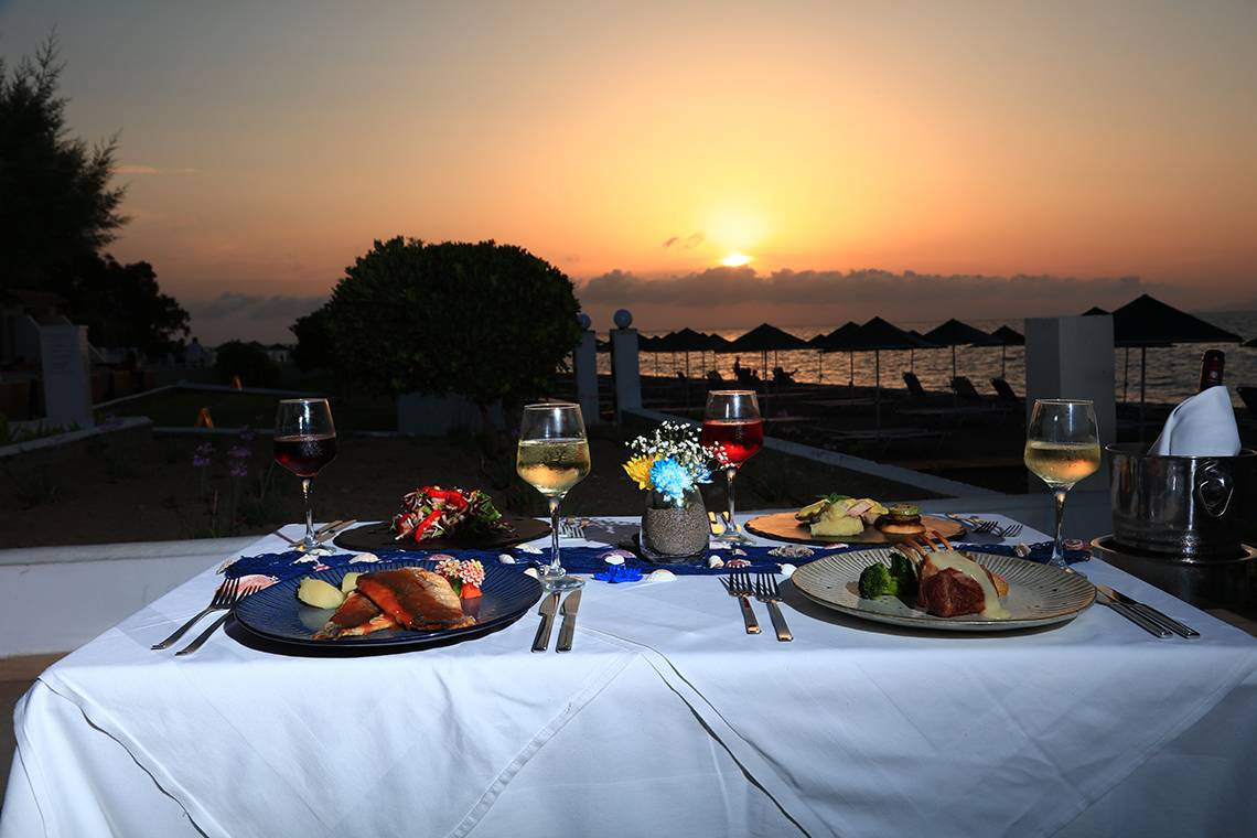 Abendessen bei Sonnenuntergang im Blue Bay Beach Resort mit Gerichten und Getränken auf dem Tisch.