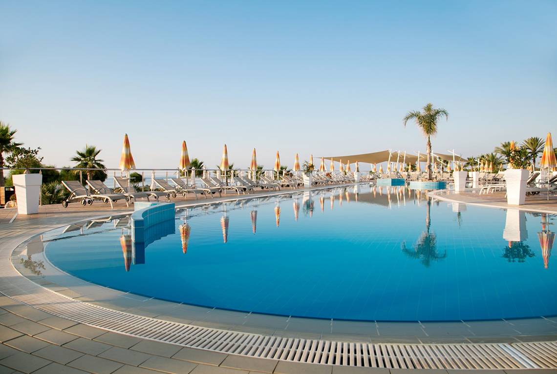 Außenpool des Asterias Beach Hotels mit Sonnenliegen und Sonnenschirmen.
