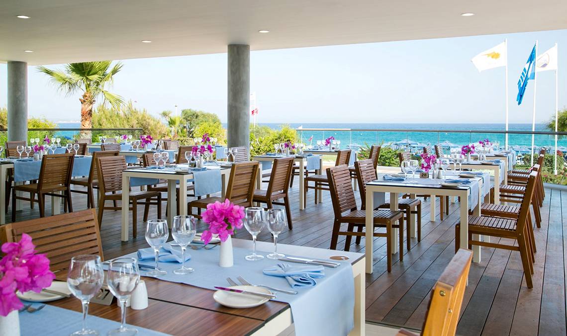 Restaurant des Asterias Beach Hotels mit Blick auf das Meer und gedeckten Tischen.