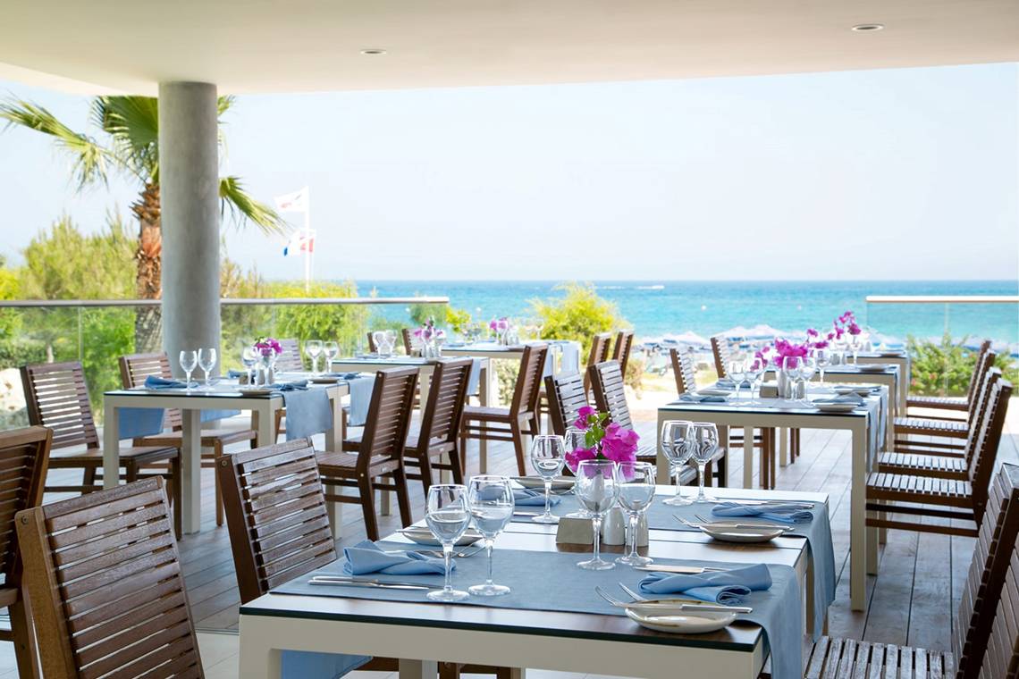 Terrasse des Asterias Beach Hotels mit gedeckten Tischen und Meerblick