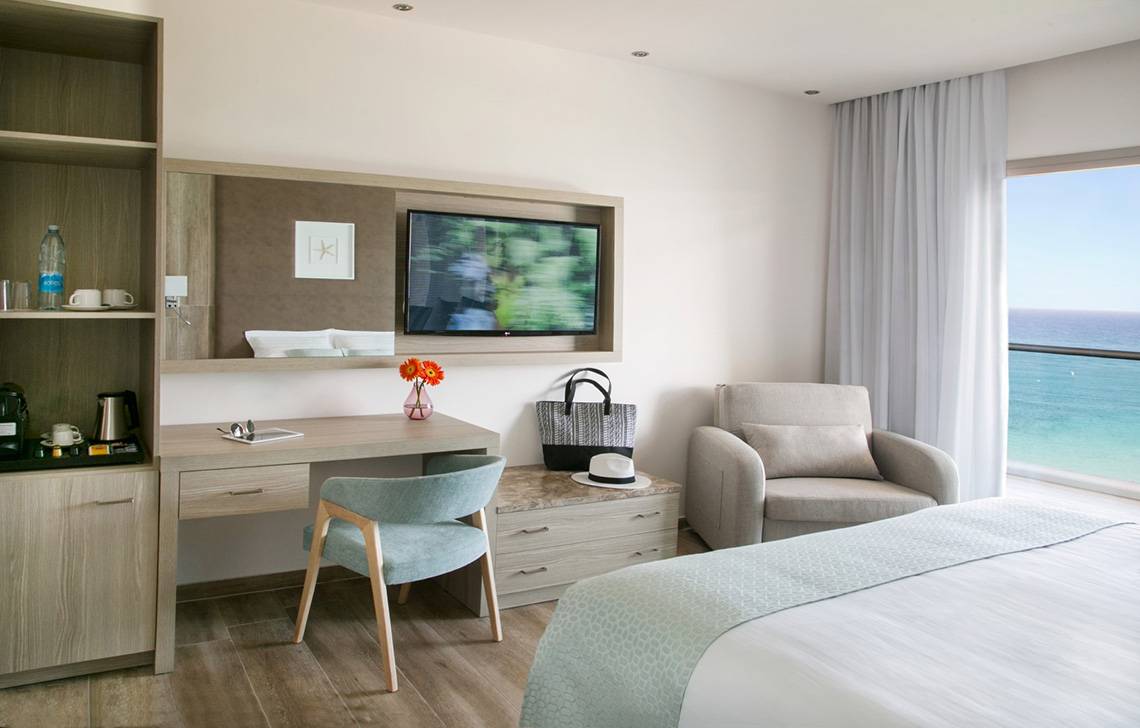 Hotelzimmer im Asterias Beach Hotel mit Bett, Schreibtisch, Stuhl und Fernseher.
