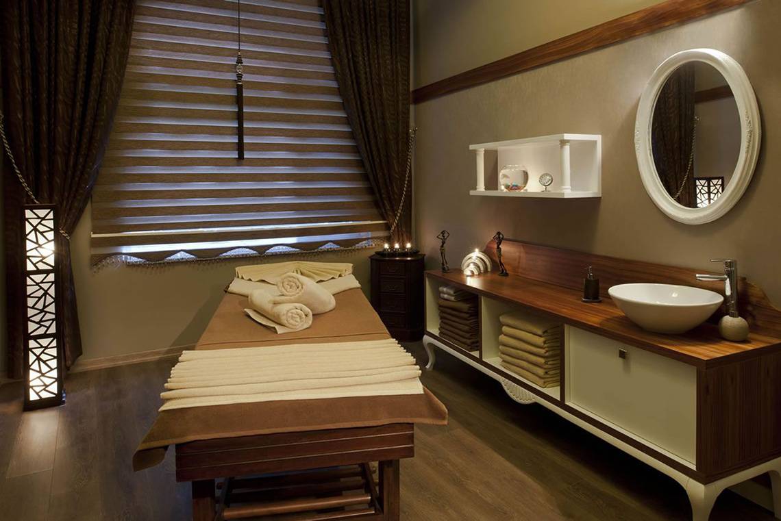 Spa-Behandlungsraum im Delphin Imperial Hotel mit Massageliege, Handtüchern und Waschbecken.
