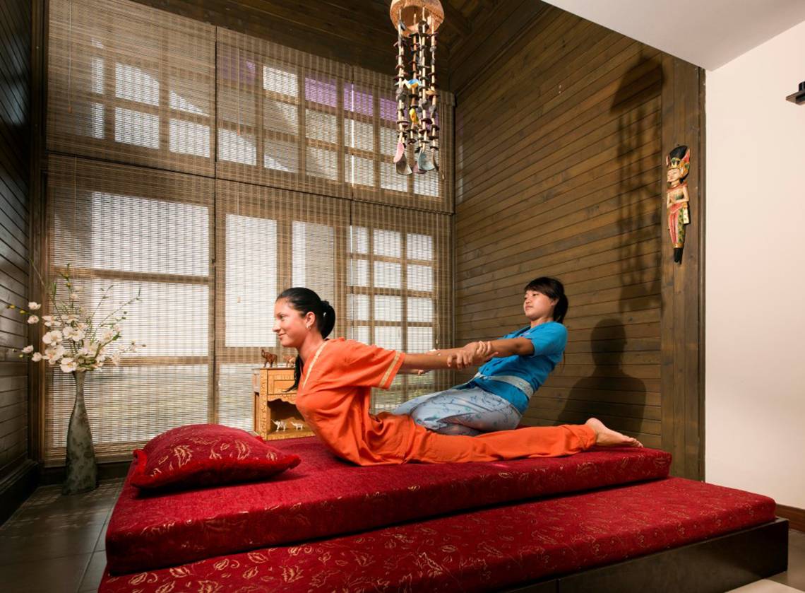 Zwei Frauen praktizieren Yoga auf einem roten Bett in einem Hotelzimmer.