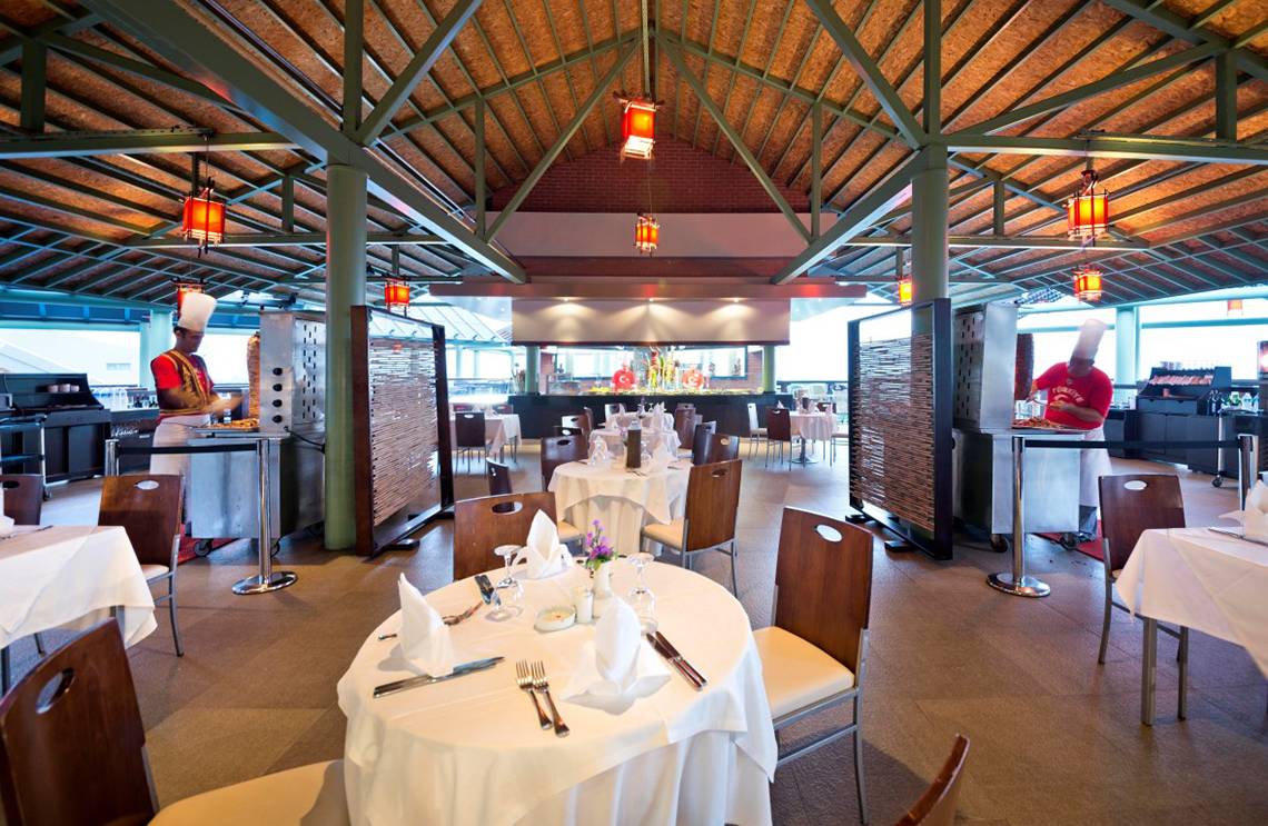 Innenbereich des Restaurants im Limak Lara De Luxe Hotel & Resort mit gedeckten Tischen und Köchen in Aktion.