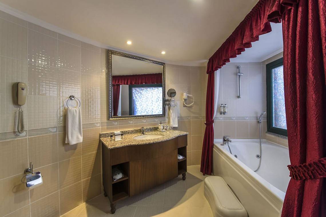 Badezimmer des Delphin Palace Hotels mit Badewanne, Spiegel und Waschbecken.
