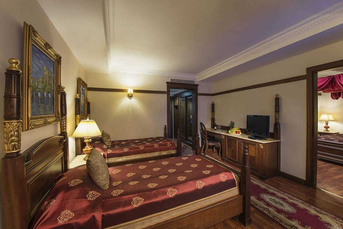 Doppelbett-Zimmer im Delphin Palace Hotel mit zwei Betten, Fernseher und Tisch mit Früchten.