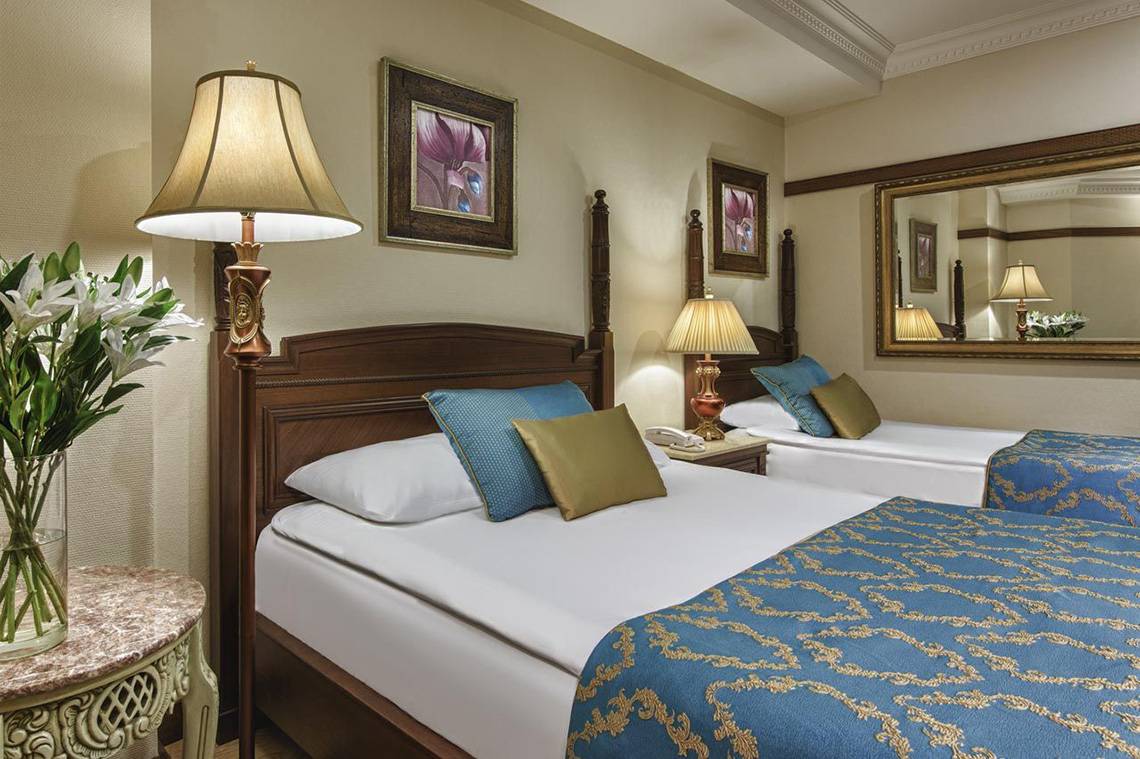 Doppelzimmer im Delphin Palace Hotel mit zwei Betten, Nachttischen, Lampen und Blumenvase.