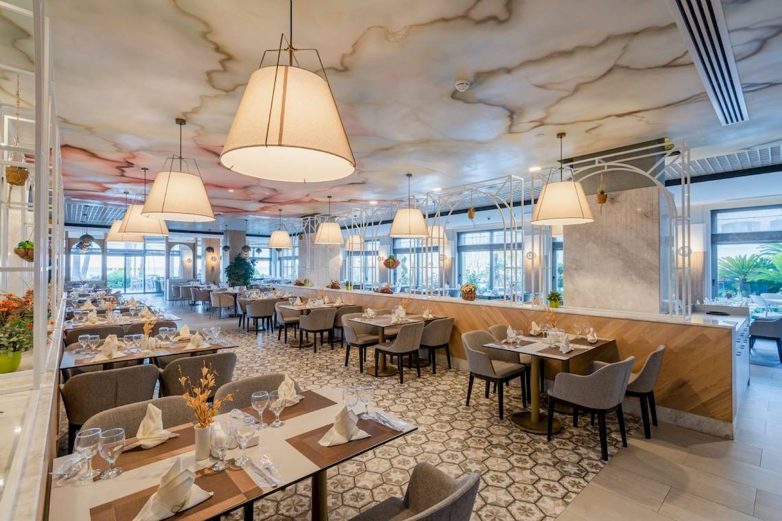 Restaurant im Fame Residence Kemer & Spa mit gemusterten Deckenleuchten und Holztischen.