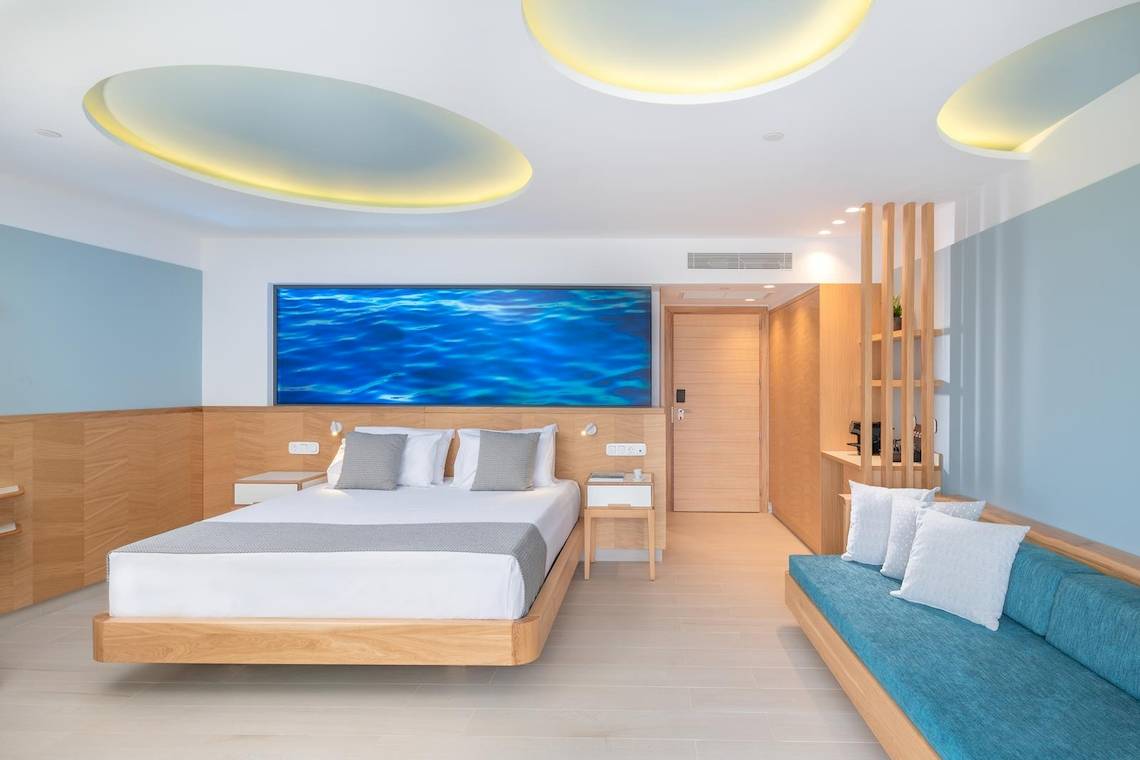 Schlafzimmer im Lyttos Mare Hotel mit einem großen Bett, einem Ozeanbild an der Wand und modernen Möbeln.