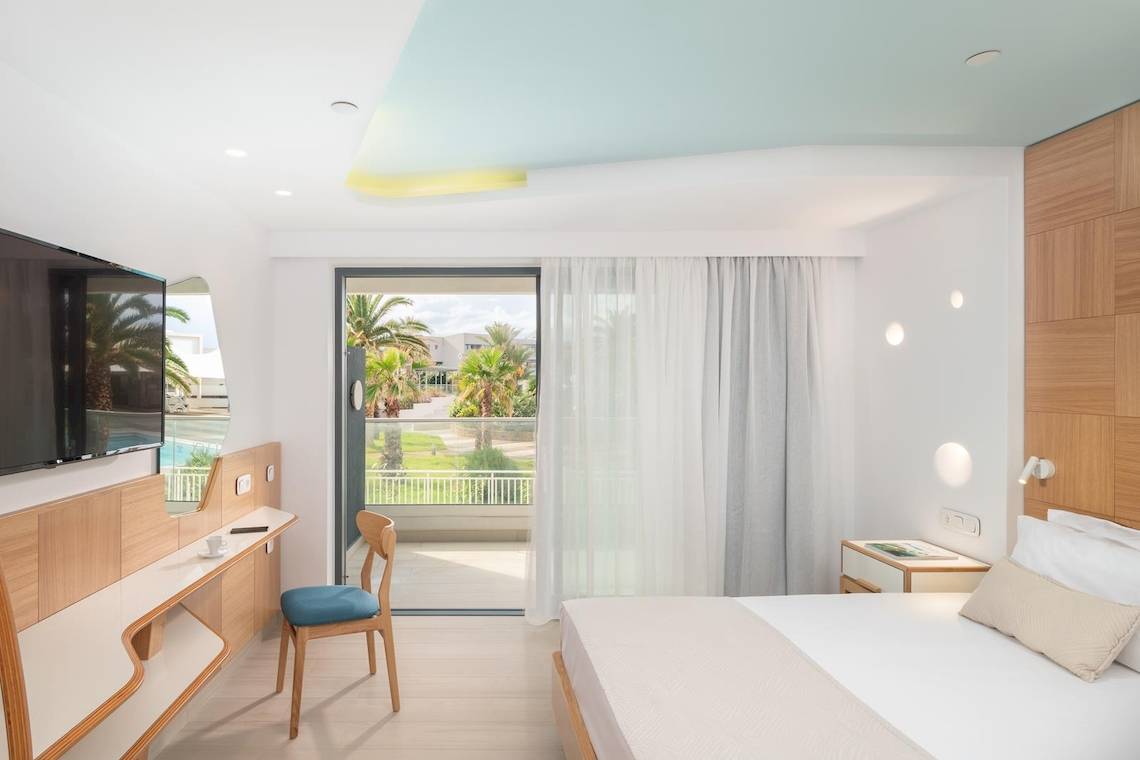 Ein modernes Hotelzimmer im Lyttos Mare Hotel mit einem großen Bett, einem Schreibtisch und einem Fernseher.