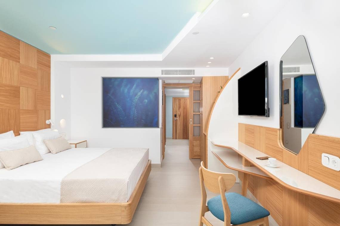 Innenansicht des Schlafzimmers im Lyttos Mare Hotel mit Bett, Fernseher und Dekor.