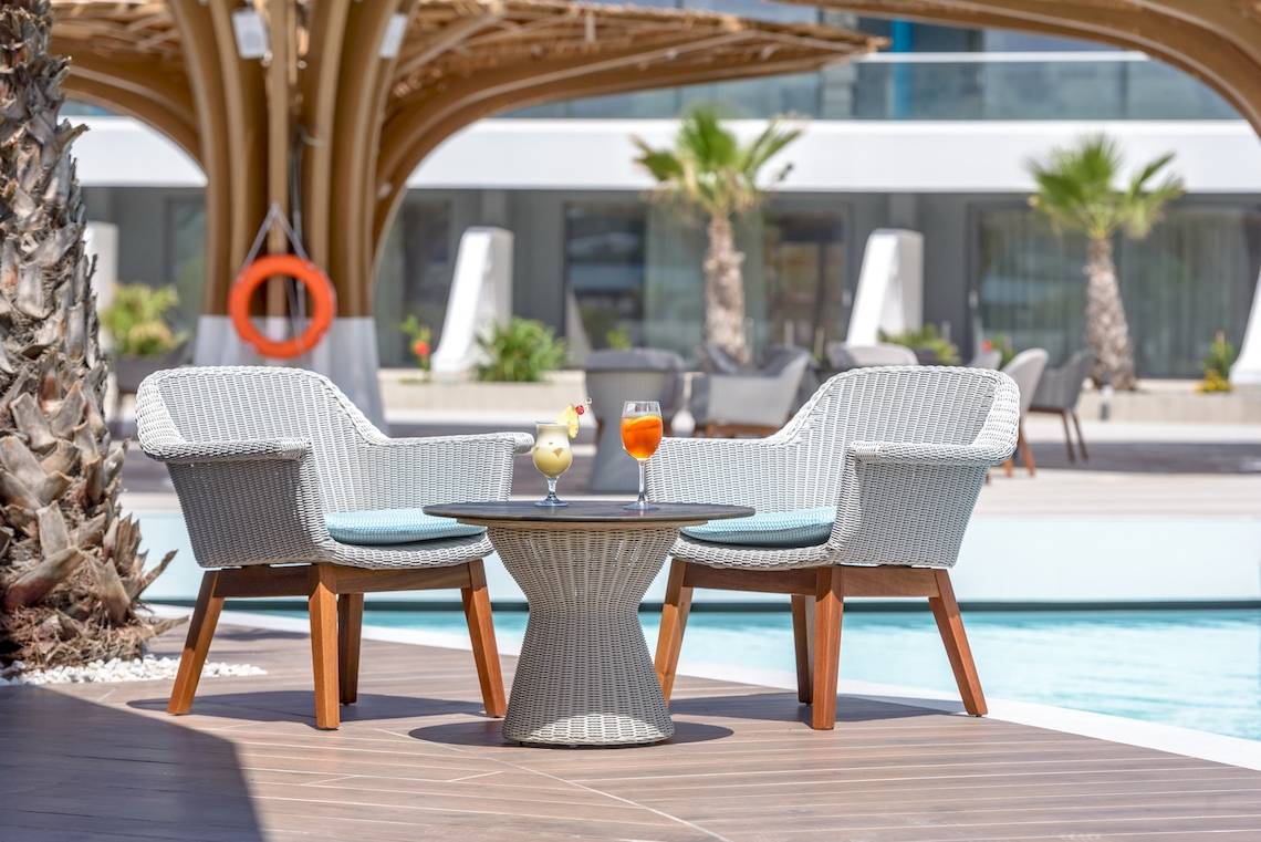 Zwei weiße Sessel mit blauen Kissen stehen neben einem runden Tisch am Pool des Lyttos Mare Hotels.