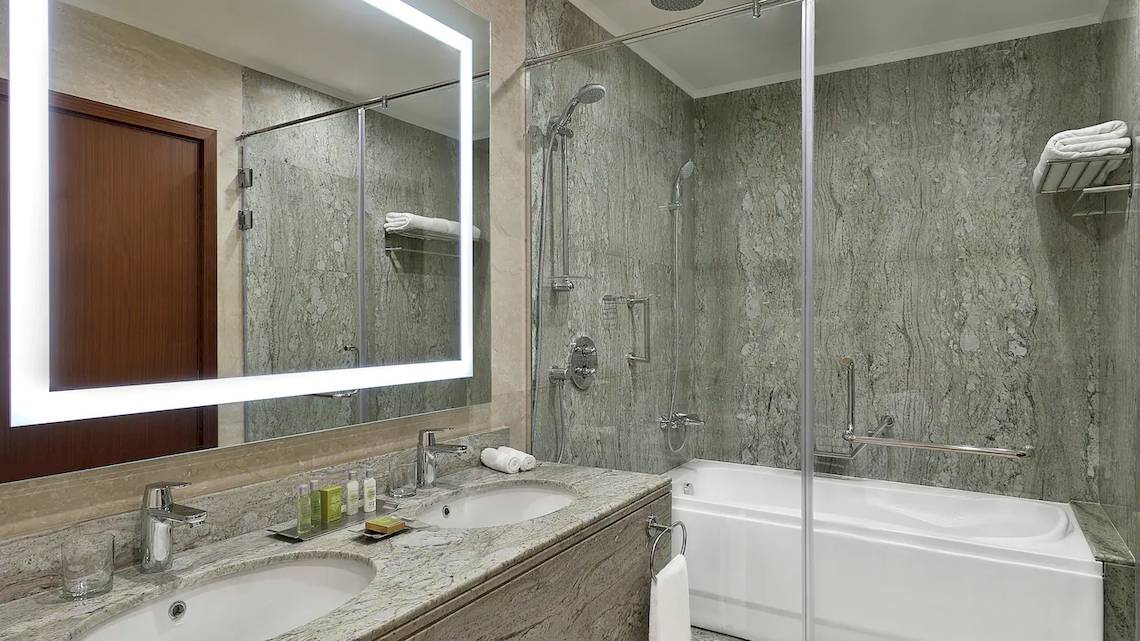 Badezimmer im Hilton Hurghada Plaza mit zwei Waschbecken, einer Badewanne und einer Glasdusche.