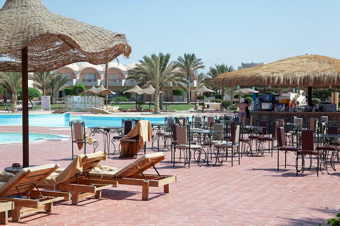 Außenbereich des Three Corners Sea Beach Resorts mit Liegen, Tischen und Sonnenschirmen neben dem Pool.