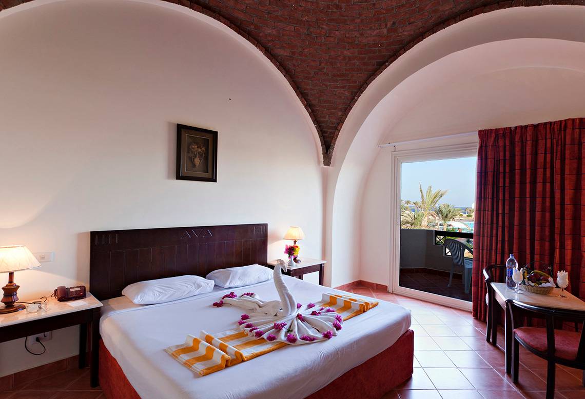 Zimmer im Three Corners Sea Beach Resort mit Bett, Tisch, Lampe und Meerblick.