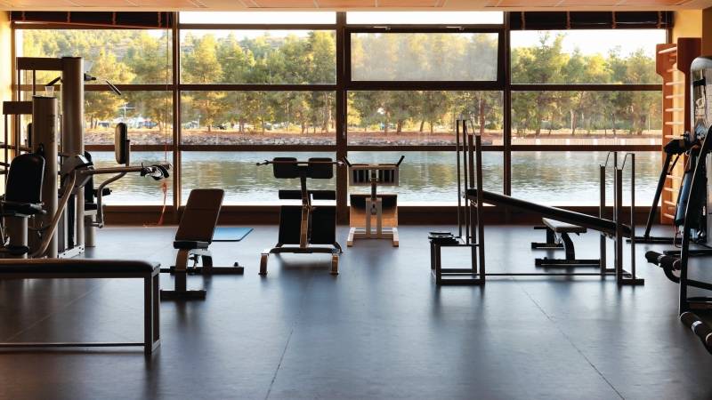 Fitnessraum im Hotel Porto Carras Meliton mit Blick auf den See und Bäumen.