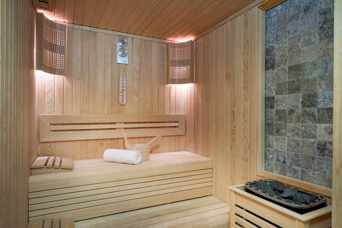 Eine hölzerne Sauna des Duja Bodrum Hotels mit einer Bank, einem Eimer und einem Thermometer an der Wand.