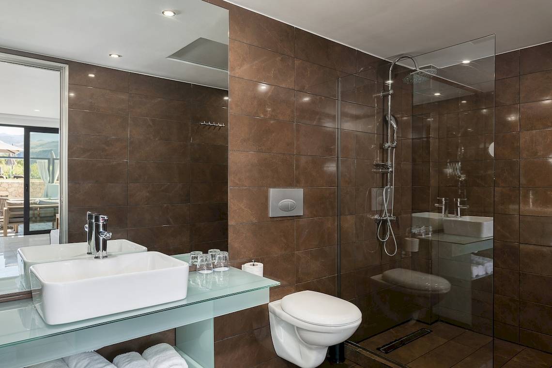 Badezimmer im CHC Galini Palace Hotel mit braunen Fliesen und Glasdusche.