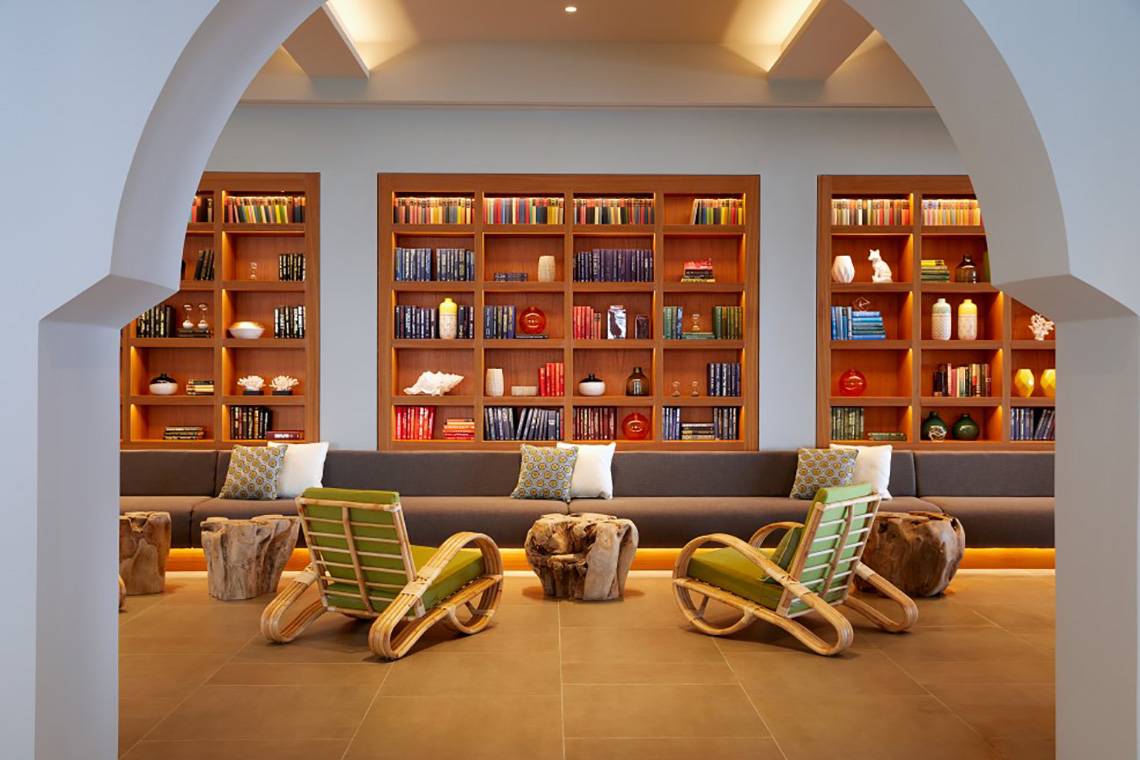 Loungebereich im MarBella Corfu Hotel mit Holzmöbeln und Bücherregalen.