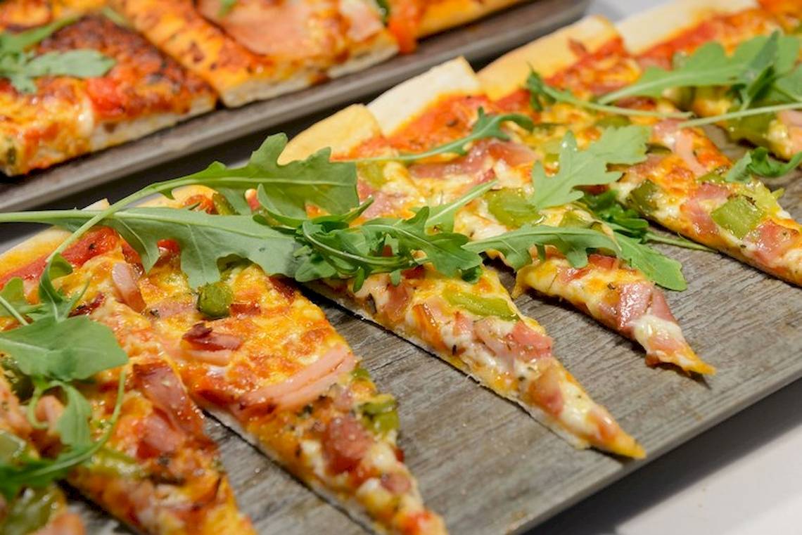 Mehrere Scheiben einer pikanten Pizza auf einem hölzernen Brett.
