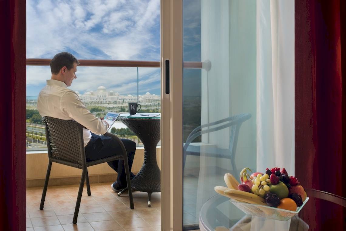 Mann arbeitet auf Balkon im Khalidiya Palace Rayhaan by Rotana mit Blick auf die Stadt