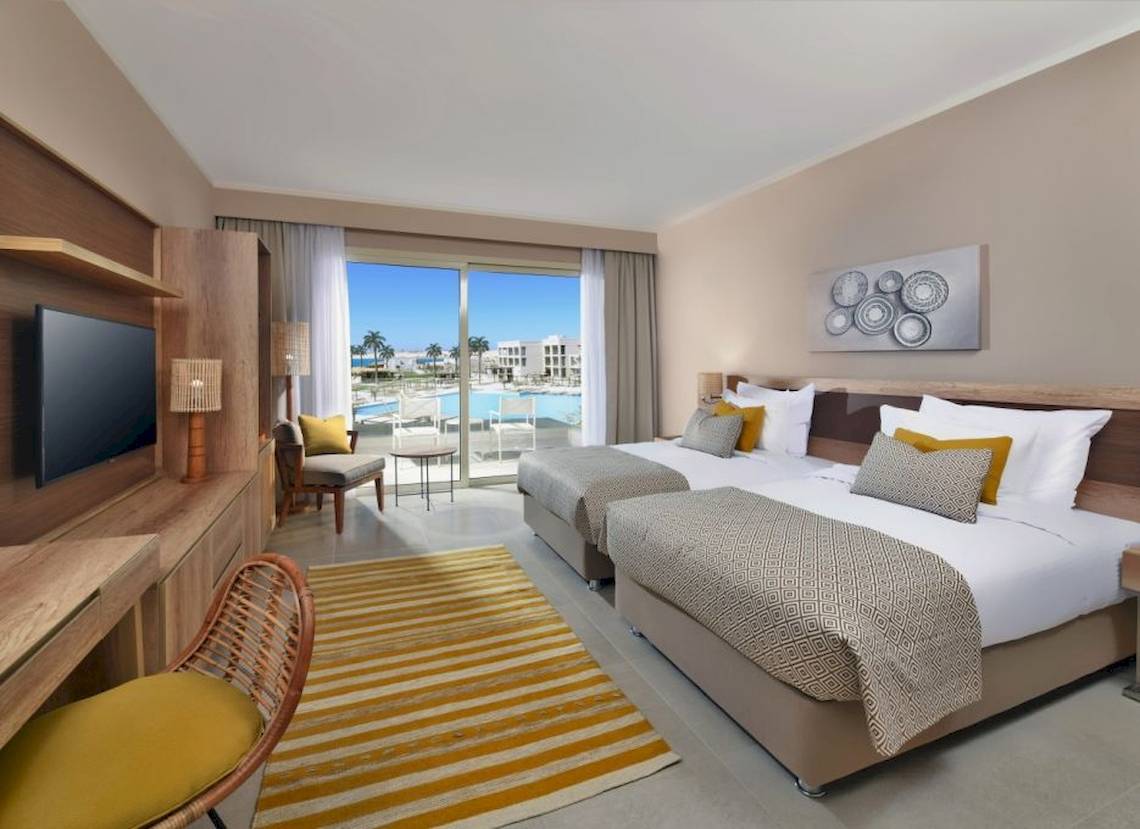 Doppelzimmer im Steigenberger Resort Ras Soma mit zwei Betten, Fernseher, Tisch und Aussicht auf den Pool.