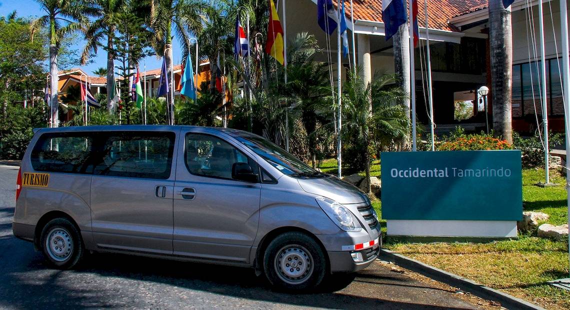 Silberner Van vor dem Occidental Tamarindo Hotel mit vielen Flaggen im Hintergrund.