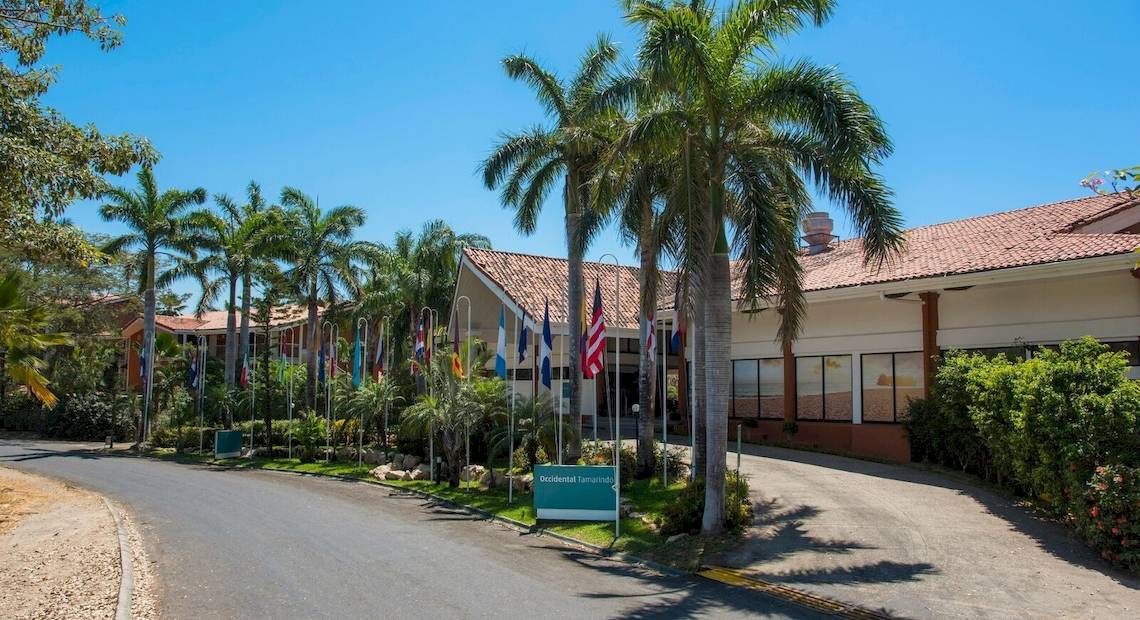 Eingangsbereich des Occidental Tamarindo Hotels mit Palmen und verschiedenen Flaggen