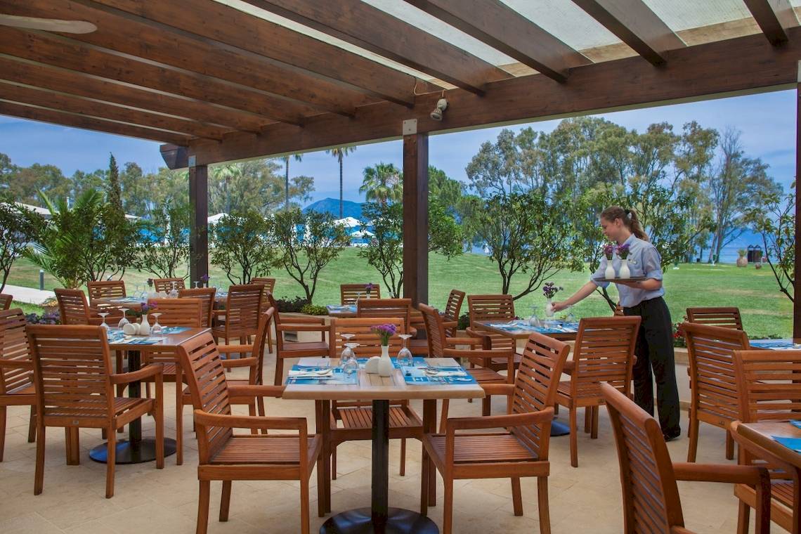 Außenbereich des Louis Kerkyra Blue Hotels mit gedeckten Tischen und Stühlen unter einer Pergola.