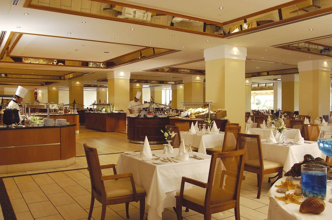 Innenbereich des Restaurants im Louis Kerkyra Blue Hotel mit besetzten Tischen und Bänken.