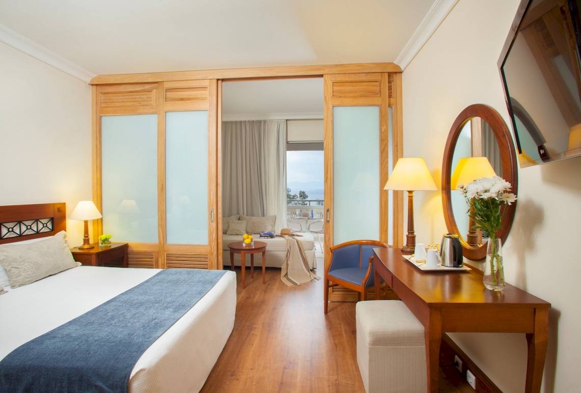 Innenansicht eines Hotelzimmers im Louis Kerkyra Blue mit Bett, Schreibtisch und Balkonzugang.