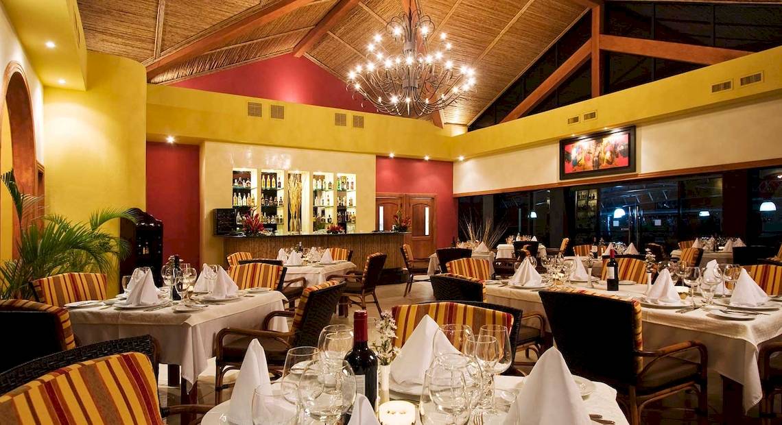 Innenansicht des Restaurants im Occidental Tamarindo Hotel mit gekleideten Tischen und einer großen Kristallleuchte.
