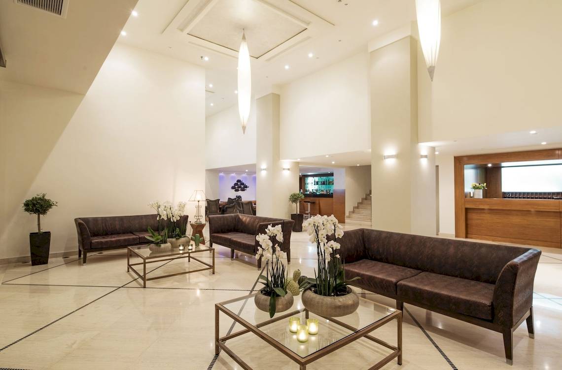 Lobbybereich des Mitsis La Vita Beach Hotels mit Sofas, Tischen und Pflanzen.