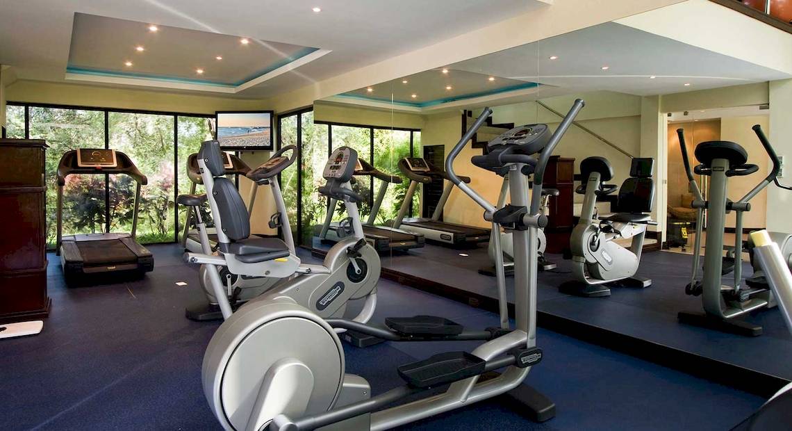 Fitnessstudio im Occidental Tamarindo Hotel mit verschiedenen Geräten und Blick auf Bäume.