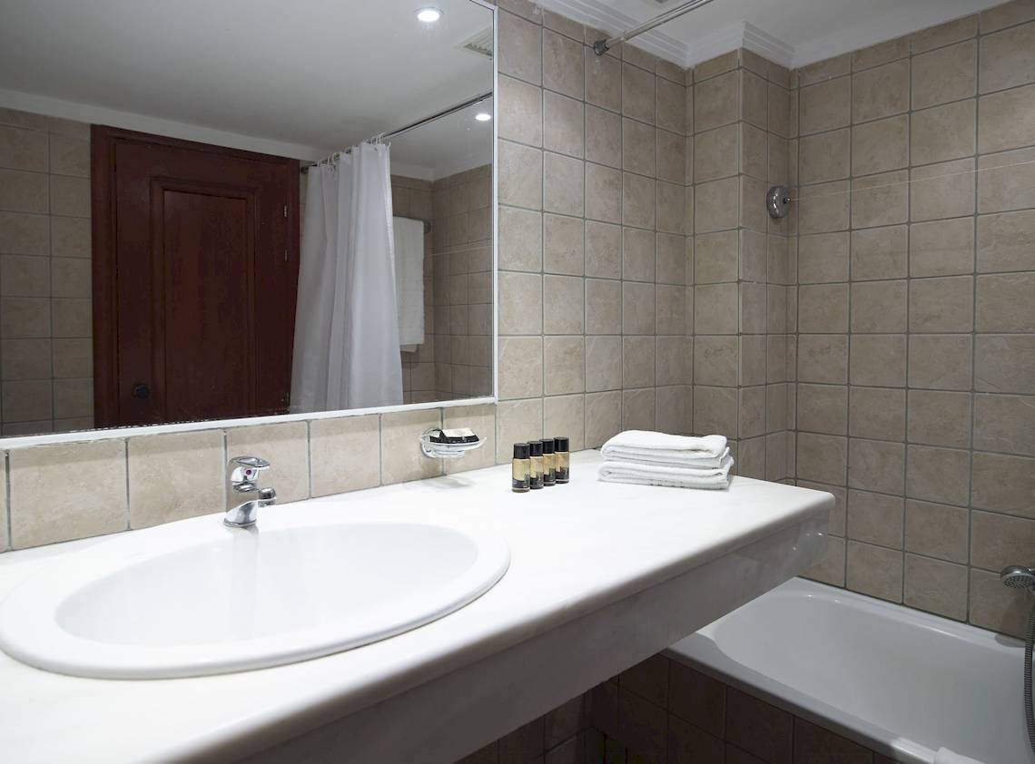 Badezimmer im Mitsis La Vita Beach Hotel mit Spiegel, Waschbecken und Badewanne.