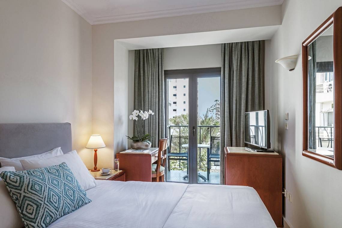 Innenansicht eines Schlafzimmers im Mitsis La Vita Beach Hotel mit Bett, Schreibtisch und Balkon
