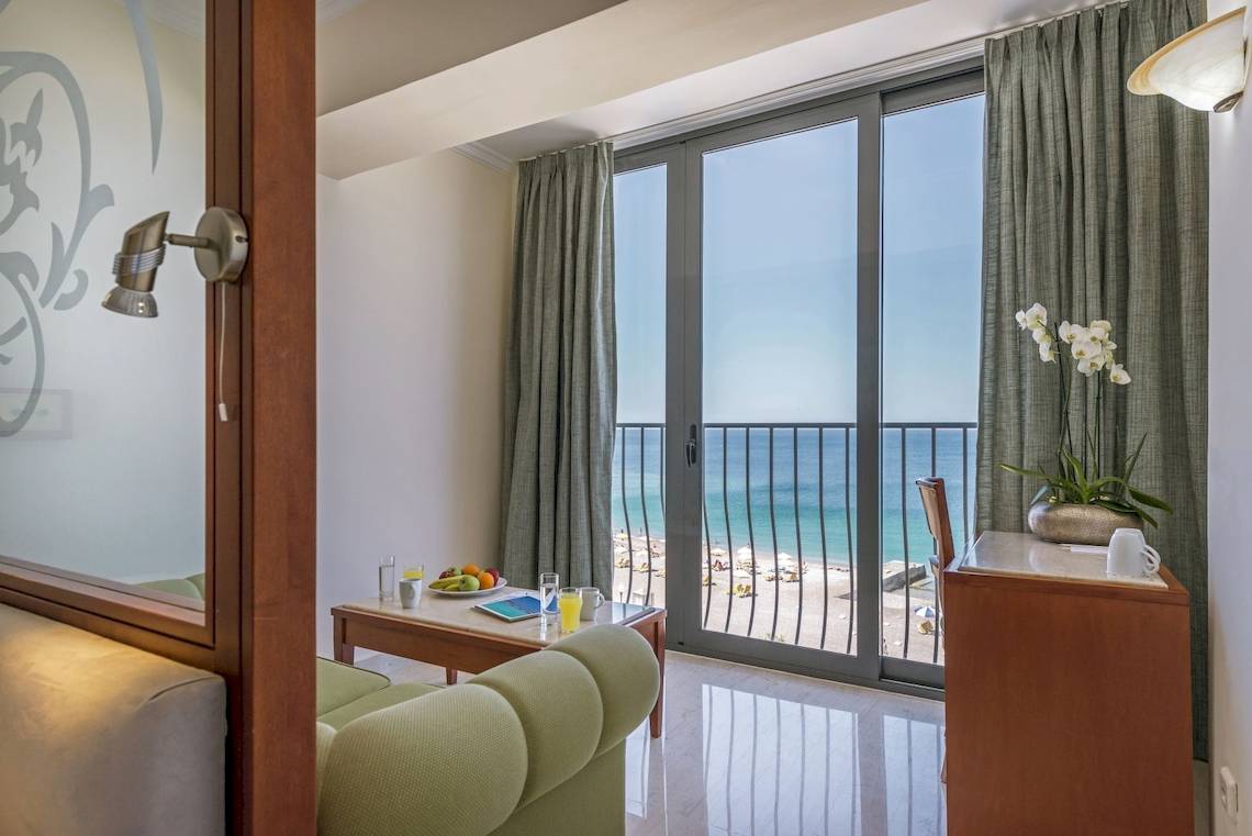 Innenansicht eines Zimmers im Mitsis La Vita Beach Hotel mit Blick auf einen Balkon und das Meer.