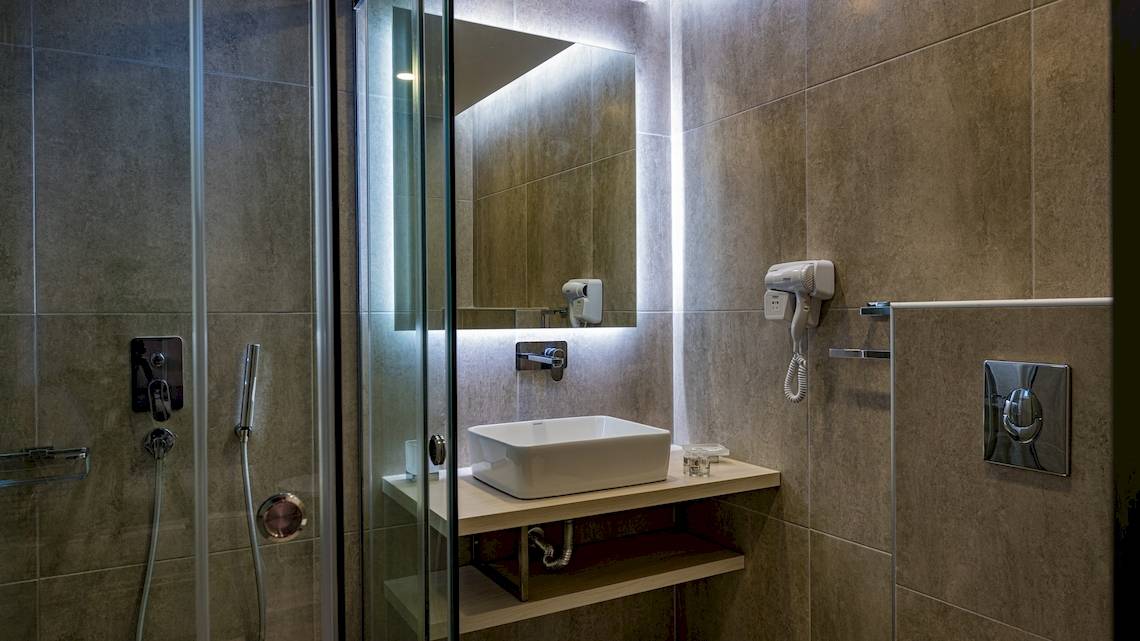 Badezimmer des Alexandra Beach Resort & Spa mit einer Glasdusche, einem Waschbecken und einem Föhn.