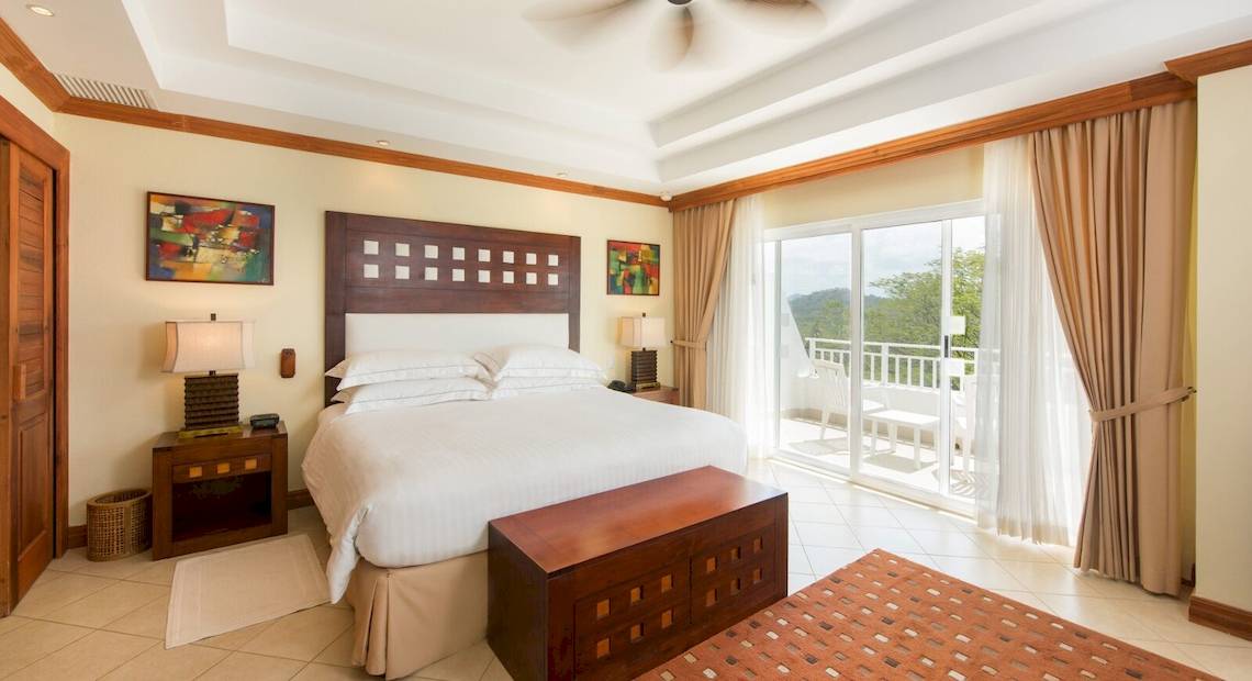 Schlafzimmer im Occidental Tamarindo Hotel mit Bett, Nachttischen und Zugang zur Terrasse.