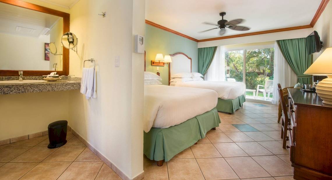 Hotelzimmer im Occidental Tamarindo mit zwei Betten, Badezimmerspiegel und Fenstern.
