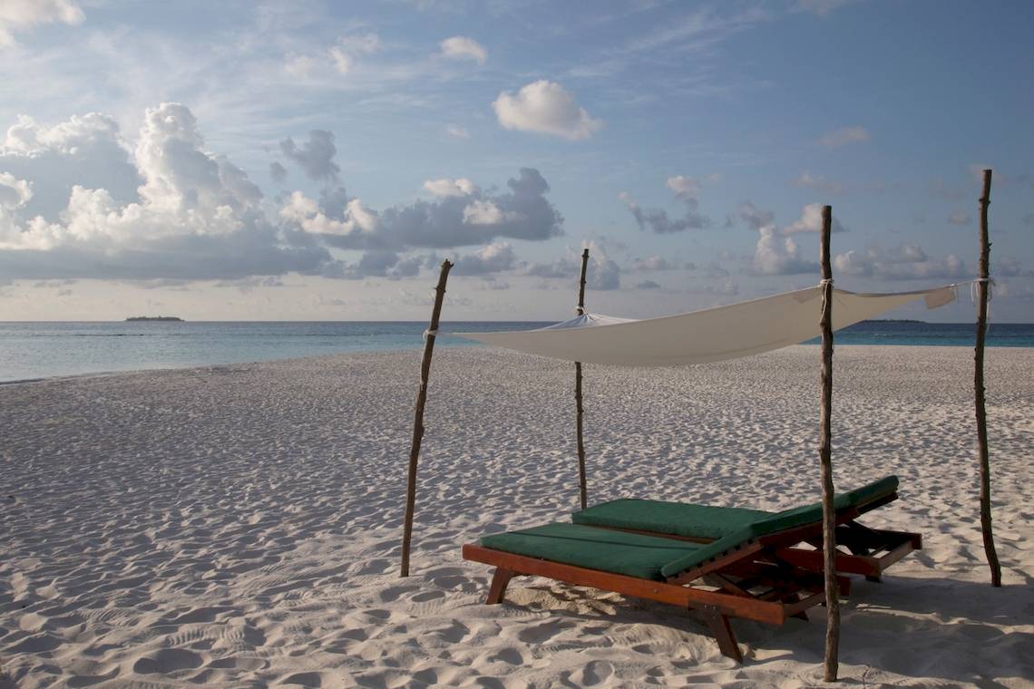 Strand des Coco Palm Dhuni Kolhu Hotels mit Sonnenliegen unter einem Segel