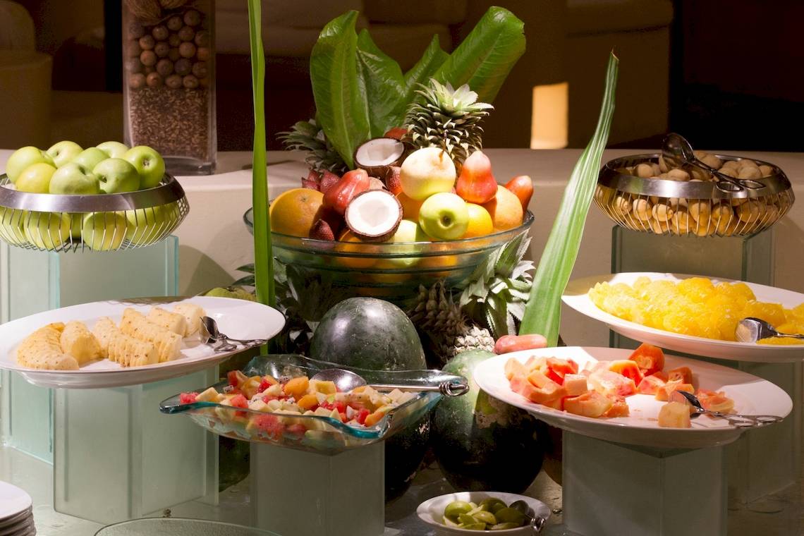 Obstteller im Coco Palm Dhuni Kolhu Hotel mit Ananas, Kokosnuss, Äpfeln und anderen Früchten.