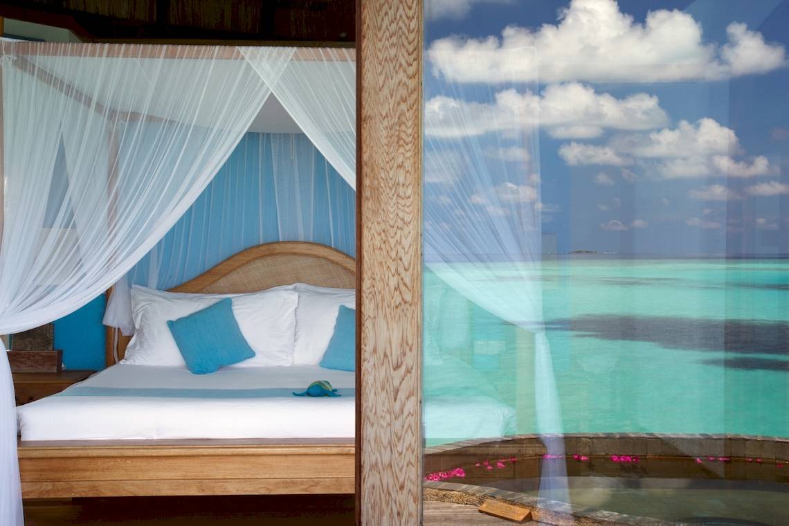 Zimmer im Coco Palm Dhuni Kolhu Hotel mit einem Bett, blauen Kissen und Meerblick.