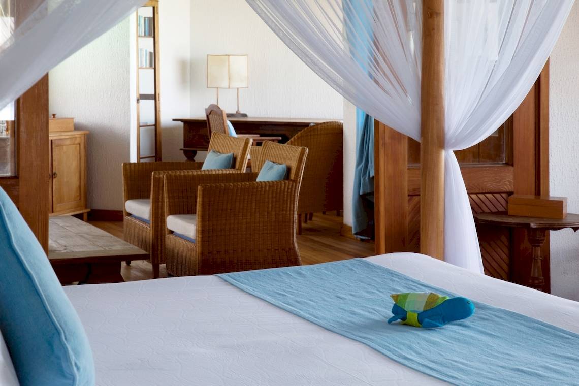 Schlafzimmer im Coco Palm Dhuni Kolhu Hotel mit vier Posterbett, zwei Stühlen, Schreibtisch und Lampe