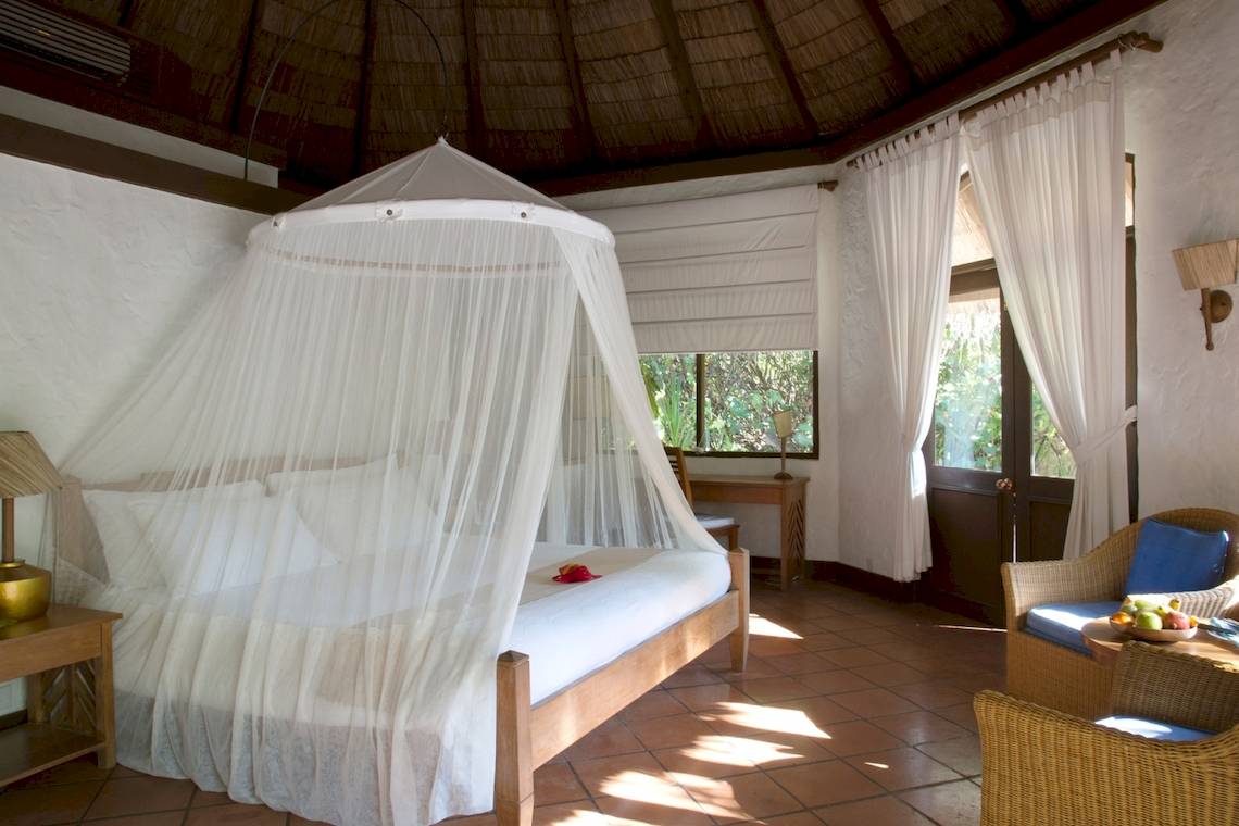Schlafzimmer im Coco Palm Dhuni Kolhu Hotel mit Moskitonetz, weißen Vorhängen und Möbeln.