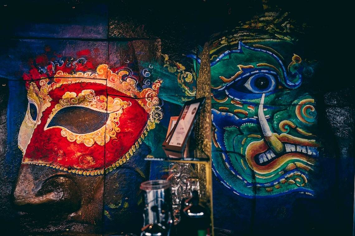 Wandmalereien im Siam@Siam Design Hotel Bangkok zeigen bunte Masken und mythische Gesichter.
