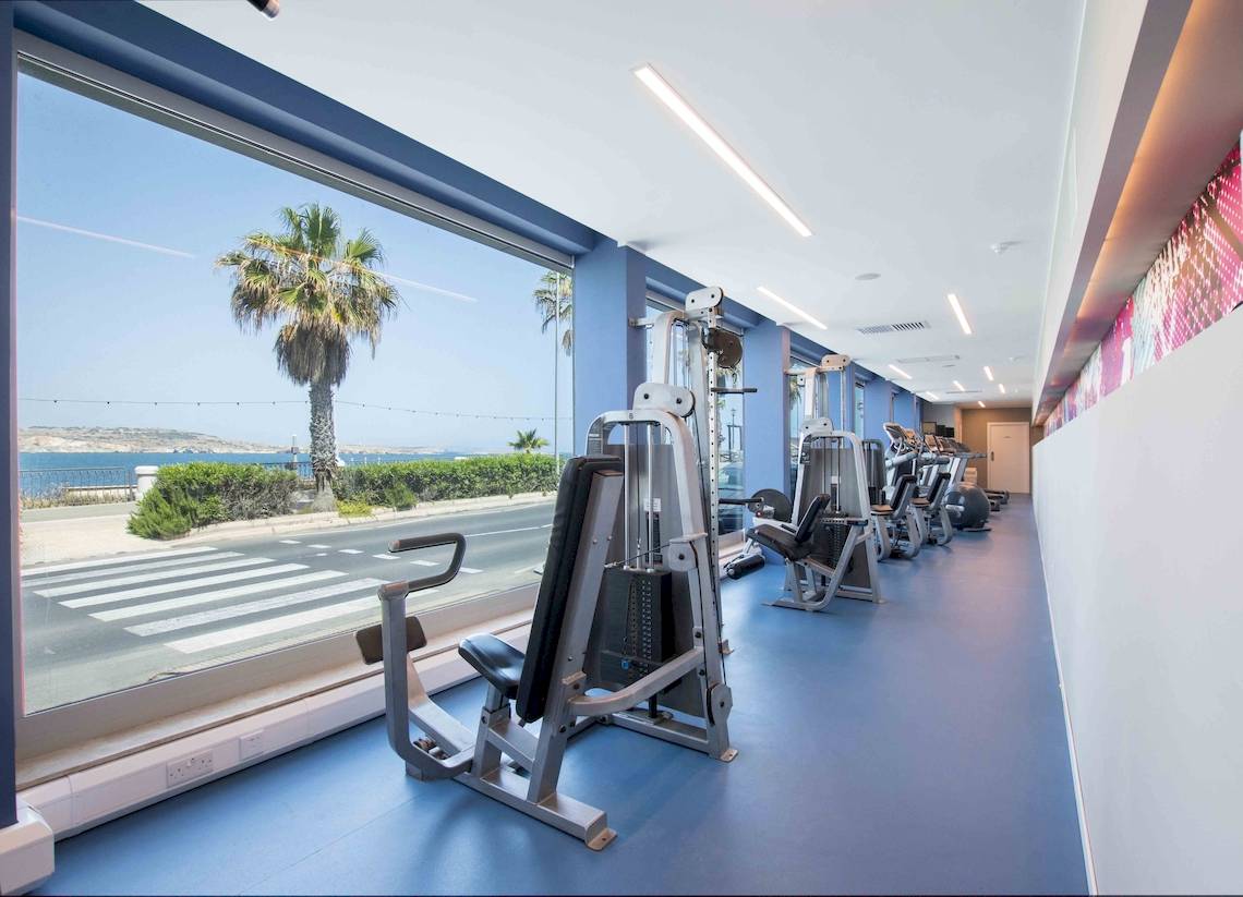 Innenansicht des Fitnesscenters im Doubletree by Hilton Malta mit Blick auf die Straße und das Meer.