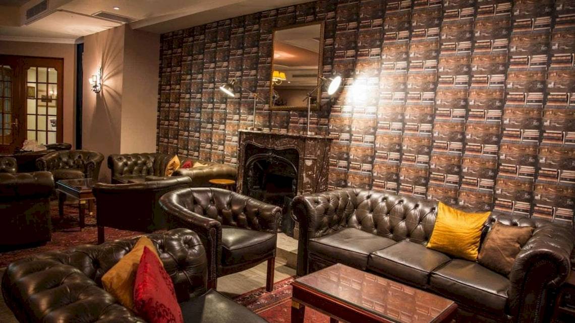 Lobby des AX The Victoria Hotels mit Ledersofas, einem Kamin und büchertapetenbedeckten Wänden.
